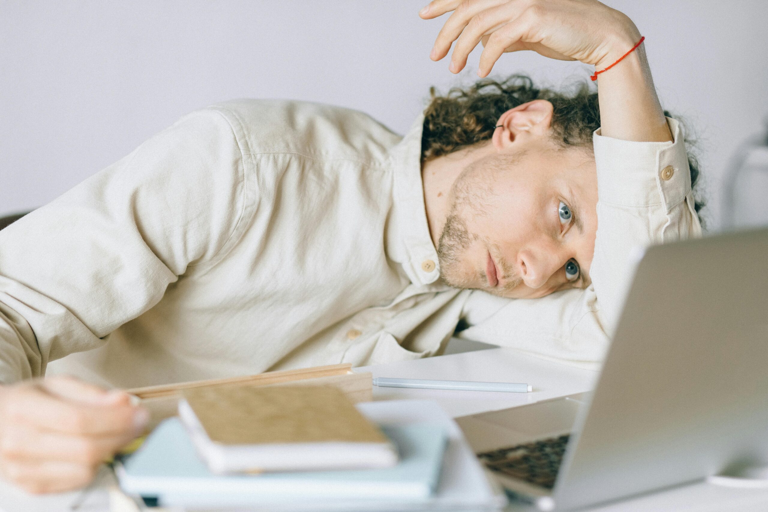 Man looking stressed with head in hands surrounded by books and laptop